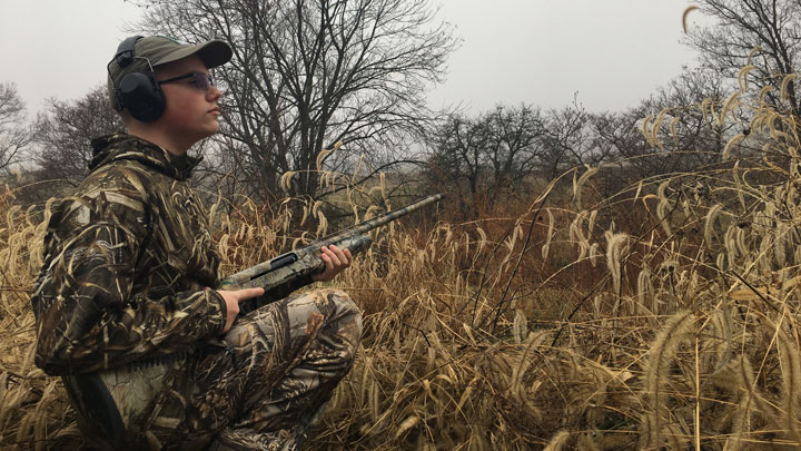 Hunter in full camo in a hay field on a cloudy day, looking skyward for birds