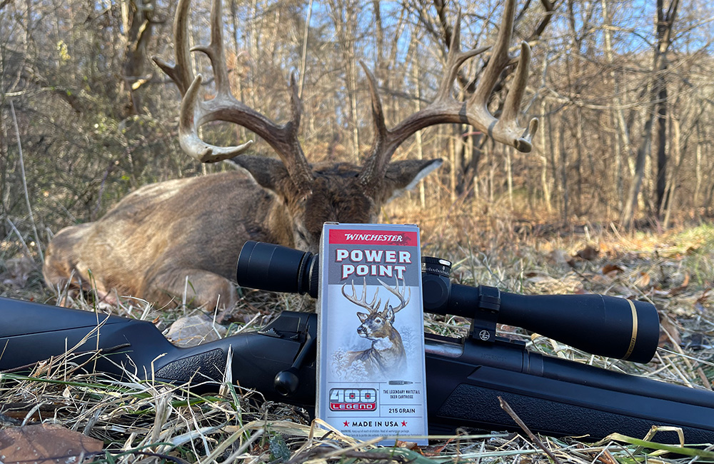 Winchester Power Point 400 Legend ammunition box resting on rifle with whitetail buck in background.