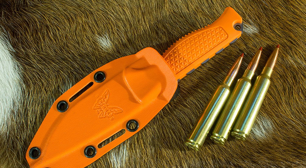 Three rounds of 300 PRC ammunition cartridges lying next to orange pocket knife.