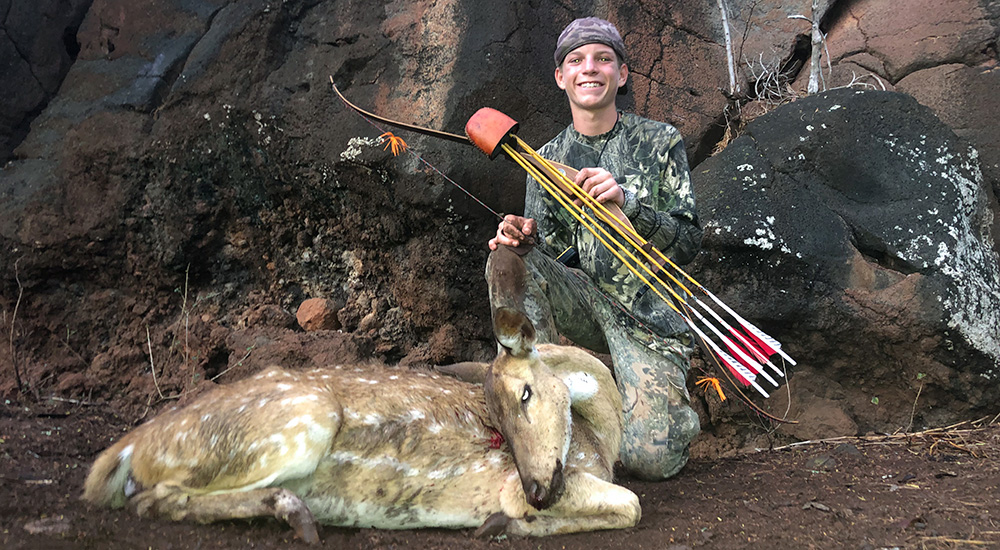 Young male hunter standing behind deer killed with traditional bow.