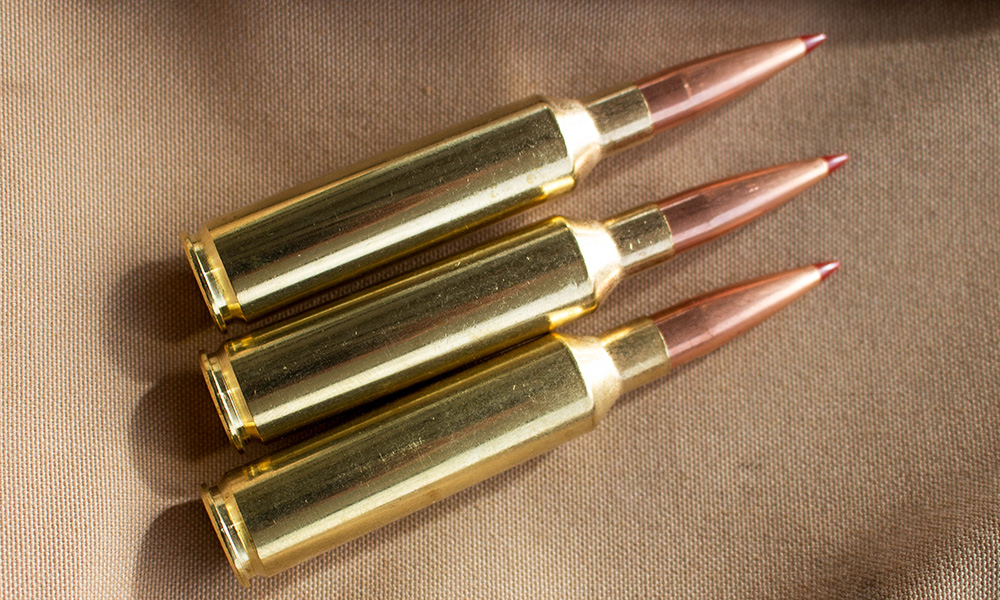 Three Hornady 7mm Precision Rifle Cartridge ammunition cartridges laying on tablecloth.