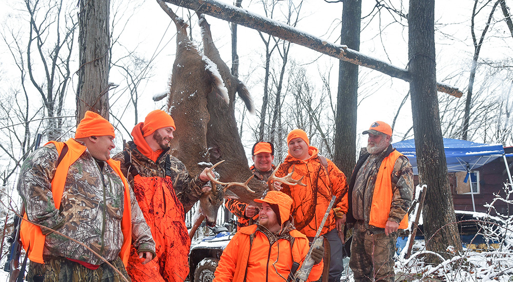 Deer hunters gathered around whitetail buck hanging from buck pole.
