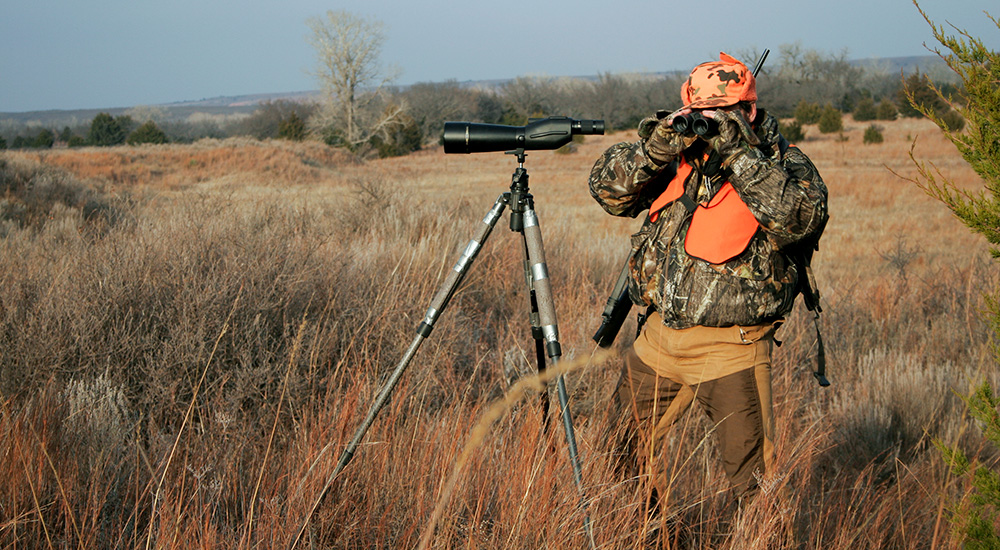 Hunter looking through binoculars in open Nebraska prairie.