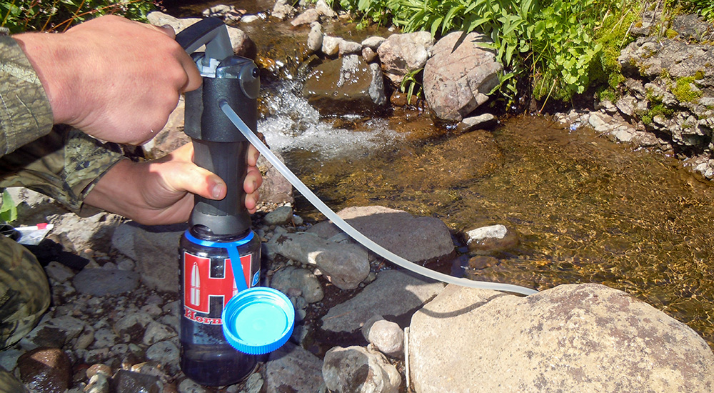 Water bottle filtration system being used to make drinking water from mountain stream.