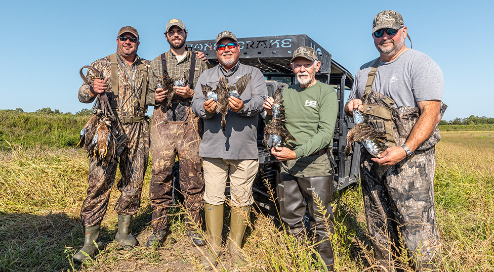 Group of duck hunters posing with ducks in tall grasses of Louisiana.