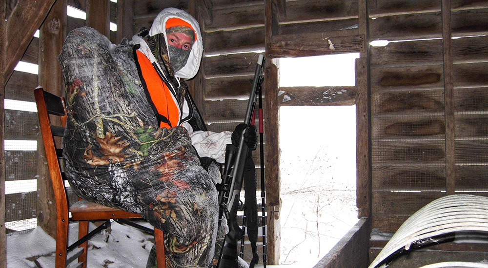 Male hunter holding rifle sitting in old wood barn.
