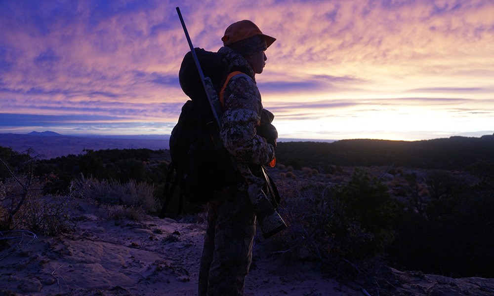 Youth male hunter standing on top of ridge with purple skyline.