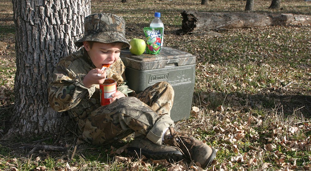 Youth Hunter Eating Lunch Against Tree