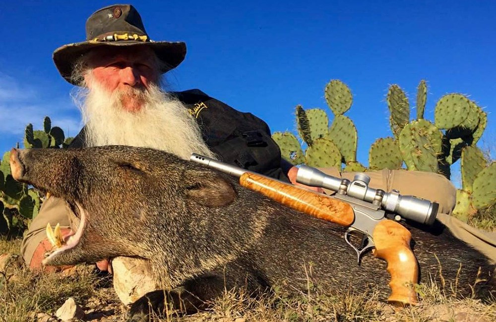 Elderly male posing with javelina and Thompson Center firearm in Texas dessert.