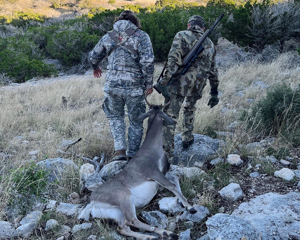 Hunters dragging whitetail buck by antlers across open field.