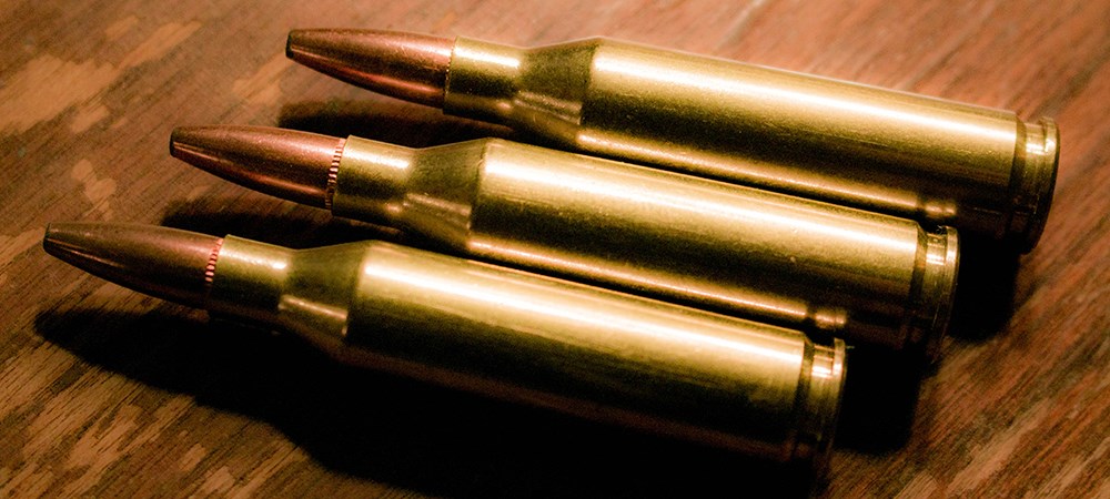 Three .243 Winchester ammunition rounds laying side by side on wood table.