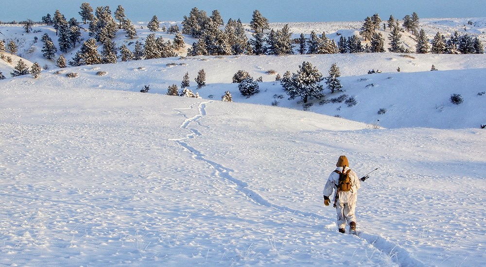 Male hunter walking on snowy mountain.