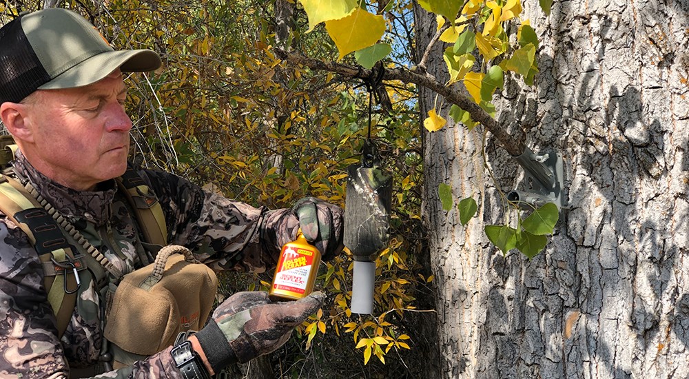Male hunter filling a deer scent dripper hanging from limb.
