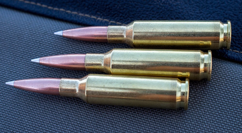 Three 6.5 Creedmoor ammunition cartridges laying on black fabric.