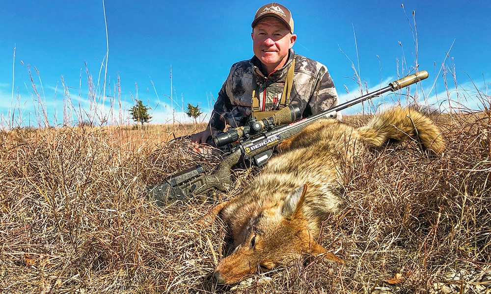 Male hunter posing with coyote in grassy area.