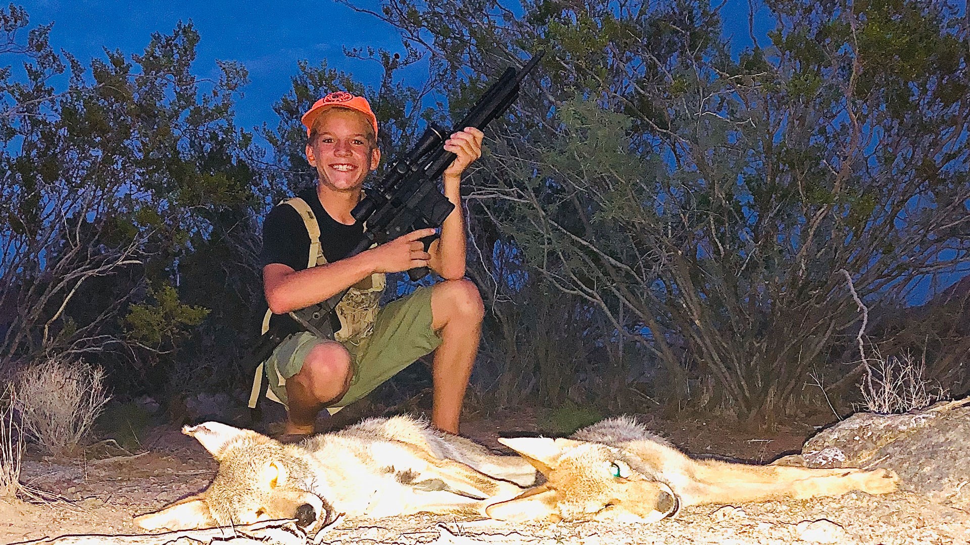 Young hunter poses on a pair of coyotes with a rifle