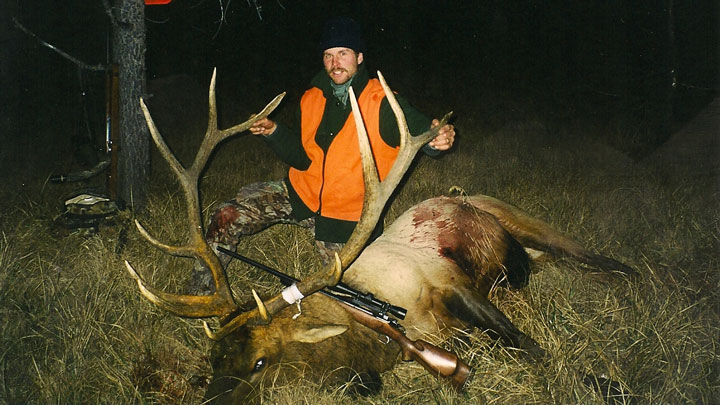 Hunter in orange poses behind an elk