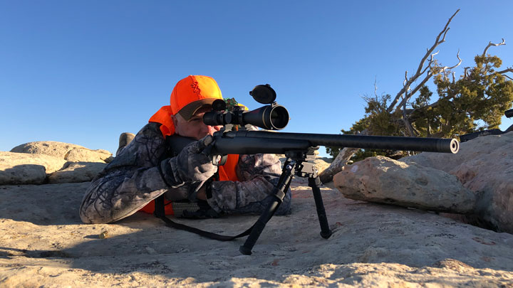 Man with rifle on tripod atop a rock