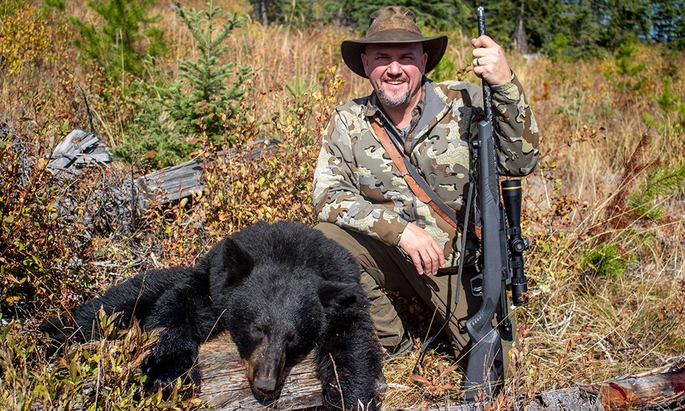 Male hunter holding straight pull rifle posing in Canada with black bear.