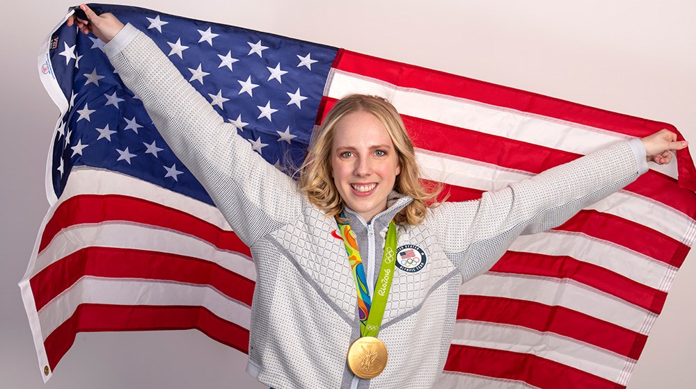 Olympian Ginny Thrasher wearing gold medal smiling while holding American flag.