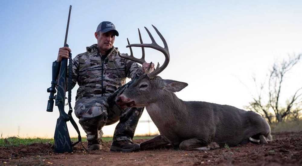 Adult male hunter posing with whitetail buck.