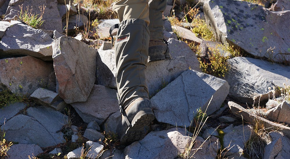 Man wearing Kenetrek books and gaiters climbing up rock hillside.