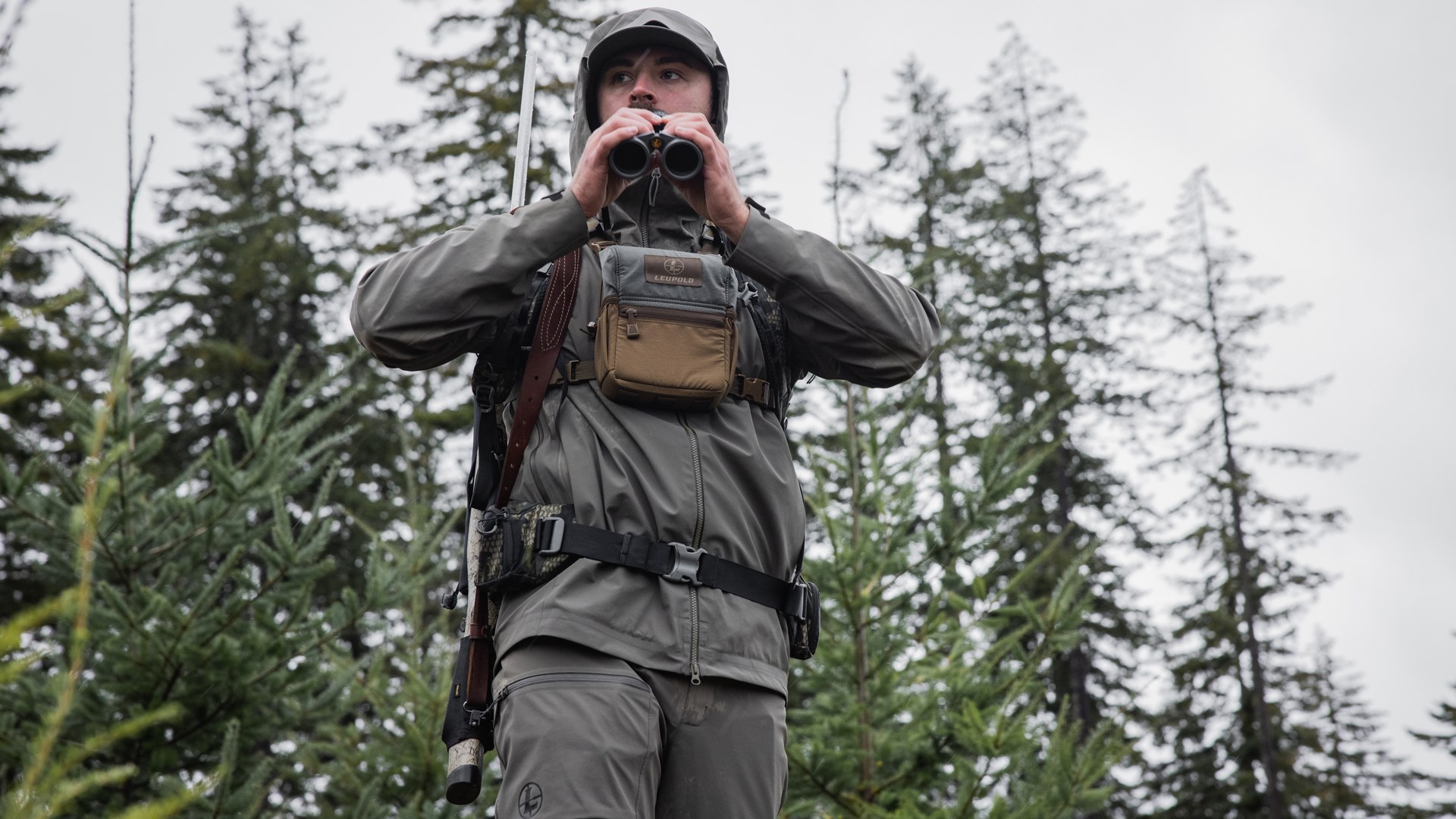 Leupold Storm Warden rain gear system man holding binoculards hilltop trees glassing outdoors in rain