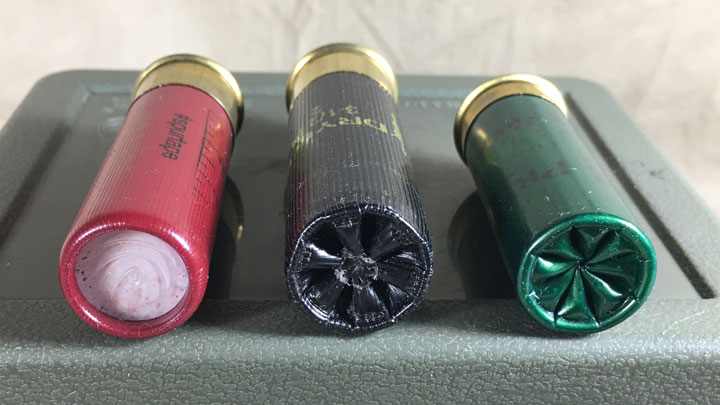 Three shotshells laying parallel with each other, ends forward. One red, one black one green (Winchester, Browning, Remington)