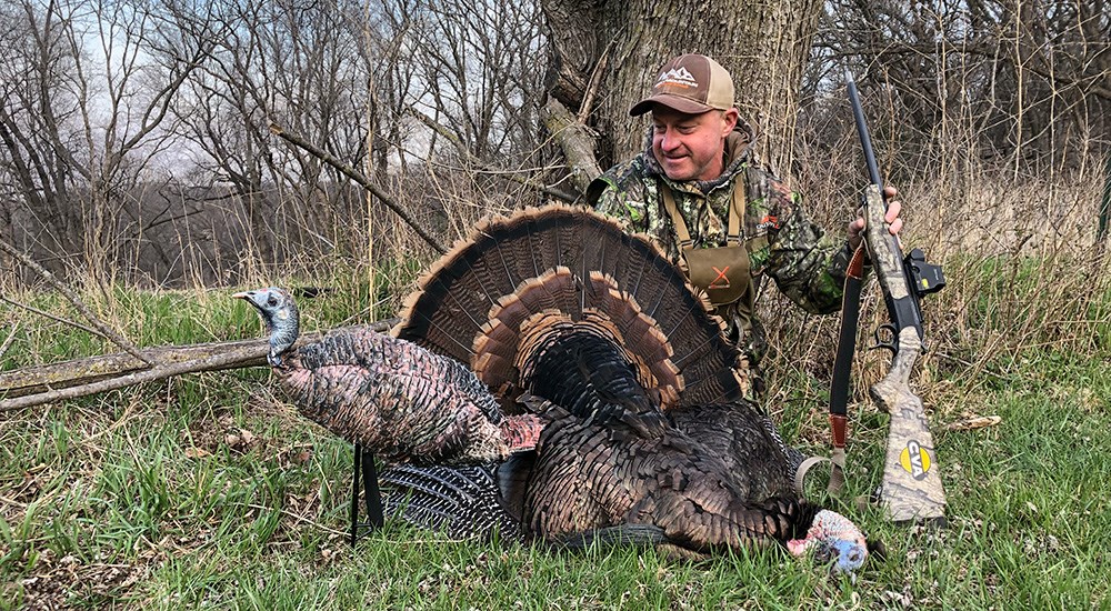 Male hunter posing with Eastern wild turkey in the woods.