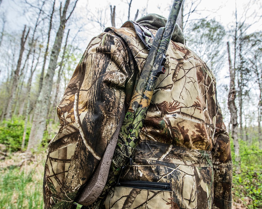 Male hunter in camouflage carrying single-shot 12-gauge shotgun on shoulder.