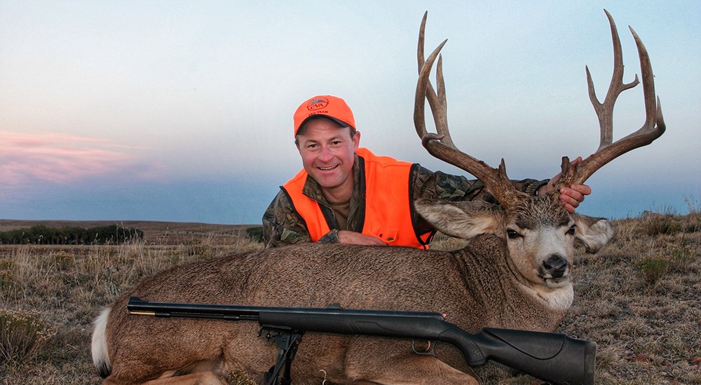 Male hunter sitting behind mule deer buck.