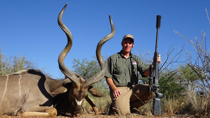Hunter poses beside a downed animal with long, screw-type horns on the African plains
