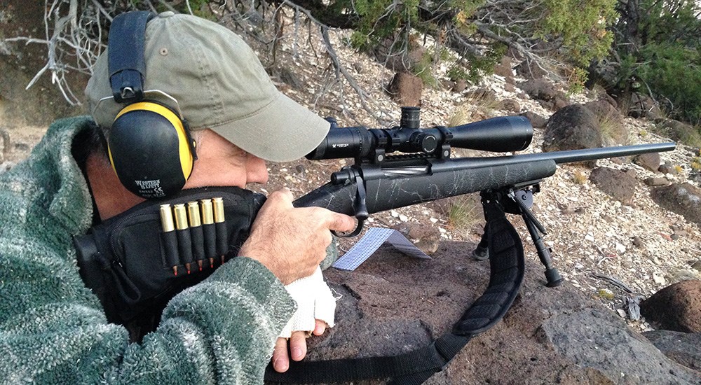 Man shooting rifle off of rock in prone position.