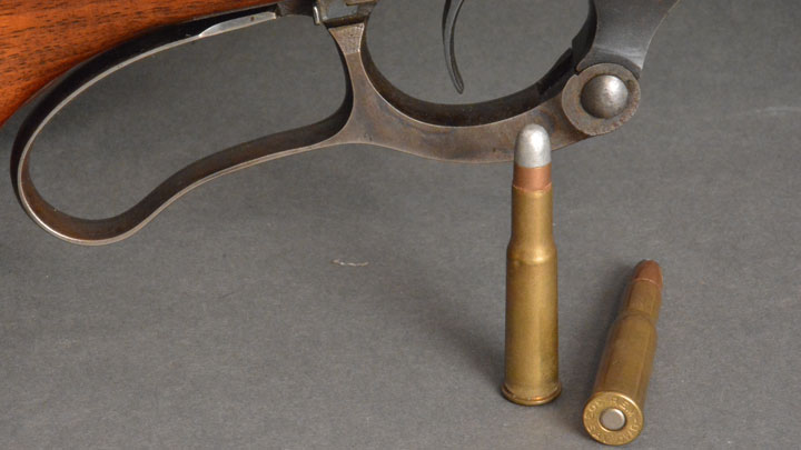 Two .303 Savage cartridges sitting next to a lever gun trigger guard