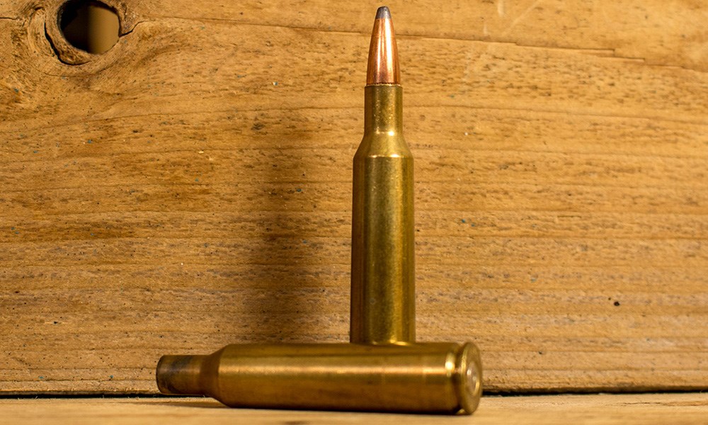 6mm Remington cartridge with a fired case laying next to it on wood table.