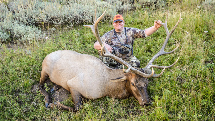 Hunter kneeling behind elk holding antlers