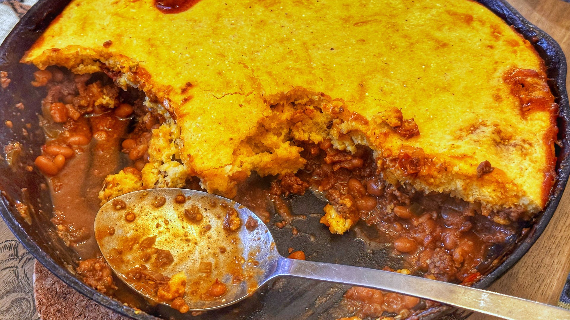 Cornbread and beans being scooped out of skillet