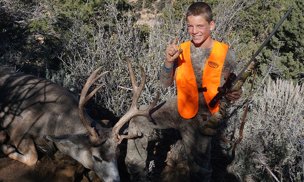 Young male hunter holding bolt action rifle posing with mule deer.