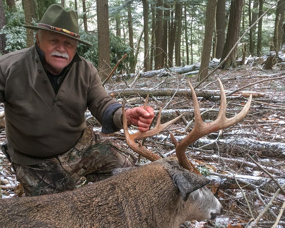 Middle Aged deer hunter with posing with whitetail buck in Vermont woods.
