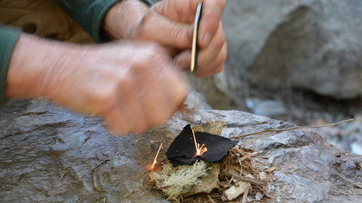 Sparks from a flint hitting the piece of char cloth in the tinder nest