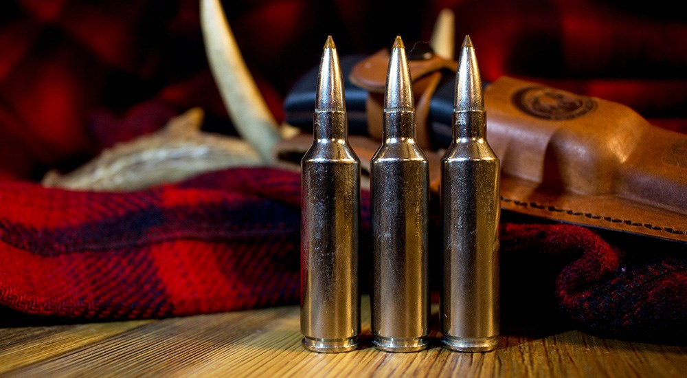 Three cartridges of .270 Winchester Short Magnum ammunition lined up on wooden table top.