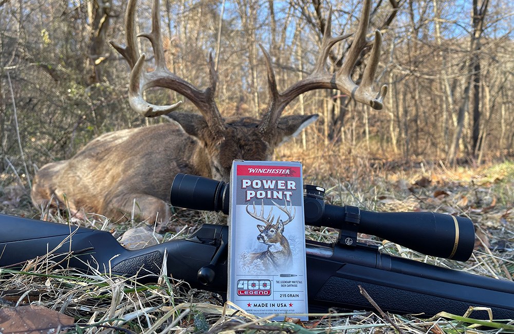 Winchester Power Point 400 Legend ammunition box resting on rifle with whitetail buck in background.