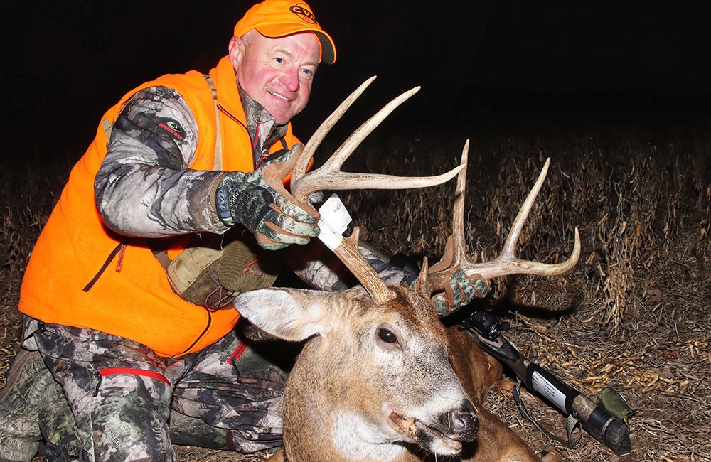 Male hunter posing with male whitetail deer in field.
