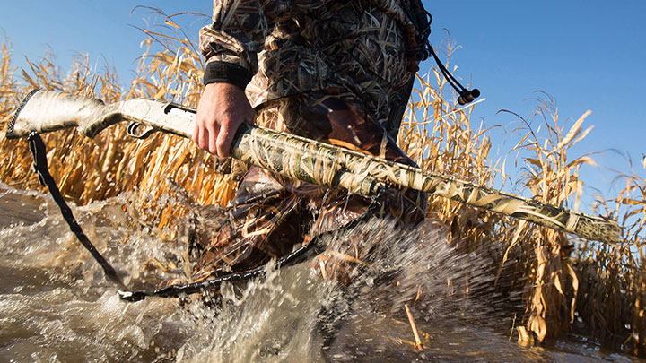 Hunter Wading Through Water Carrying Shotgun