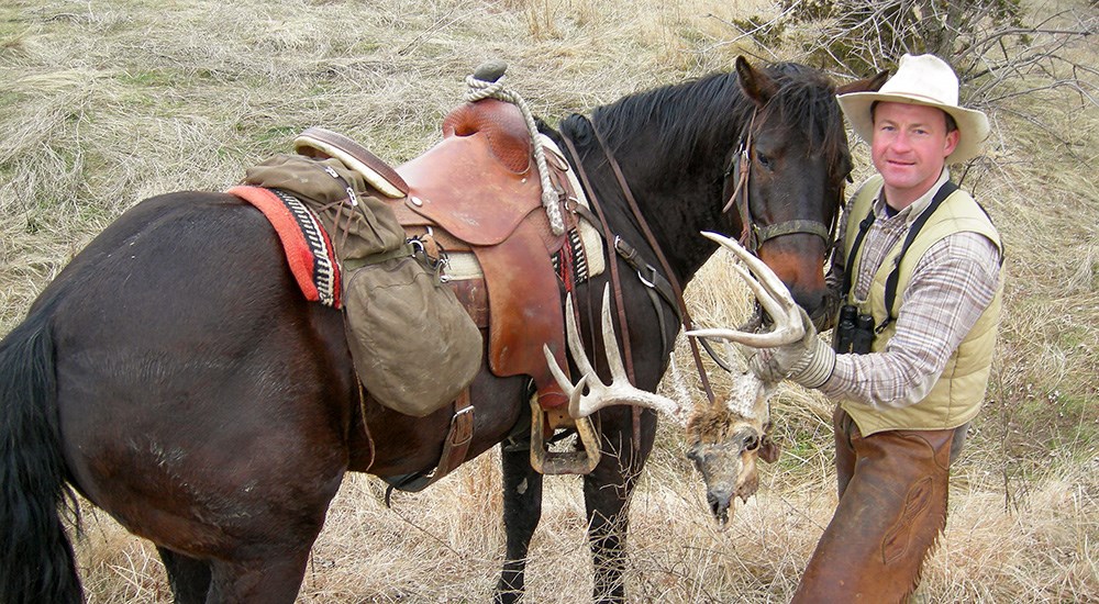 Man with horse holding whitetail deer skull found while riding.