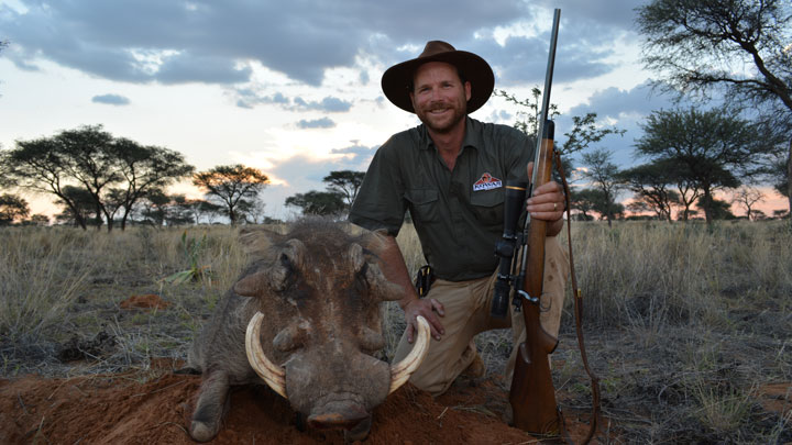 Author posing with a warthog with a beautiful sunset behind