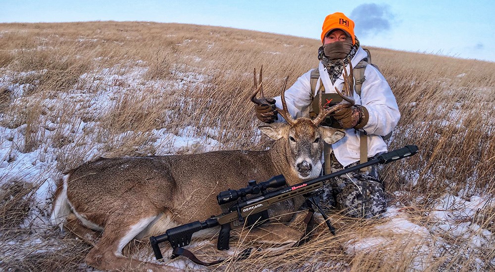 Hunter posing with whitetail buck in open field.