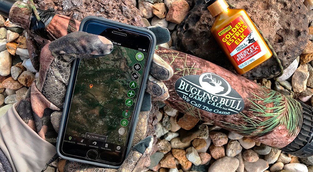 Hunting app open on cell phone screen laying next to bugling bull game call.