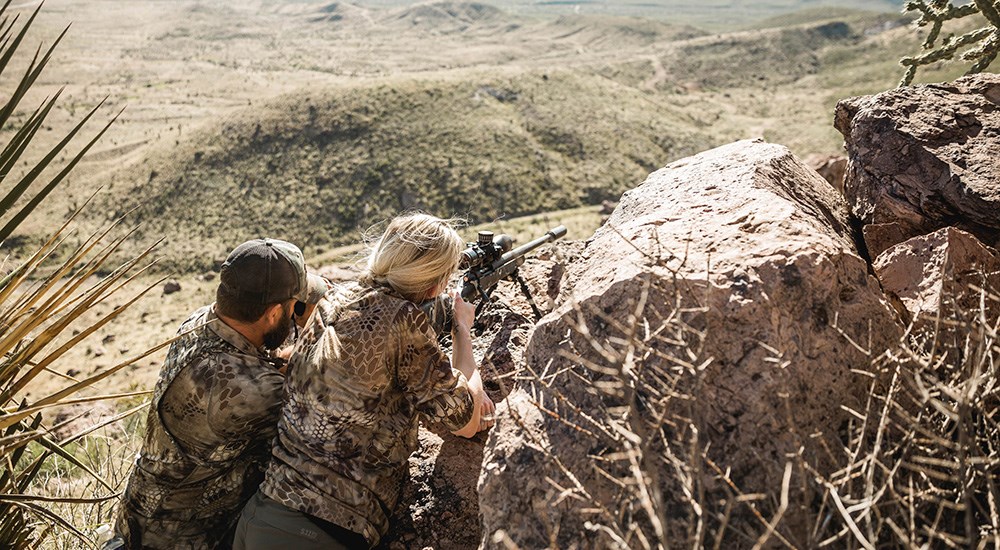 Female hunter resting rifle on rock preparing for shot on Texas aoudad.