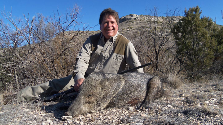 Hunter leans behind a javelina he has shot, dry mesa in the background